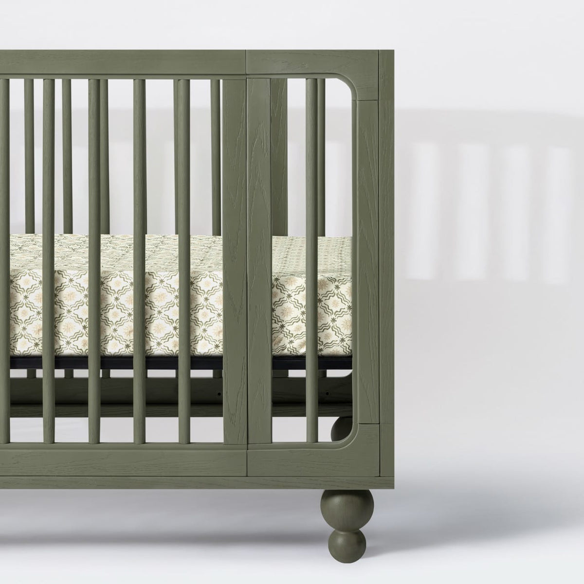 Babyletto olive green wooden crib with patterned mattress sheet