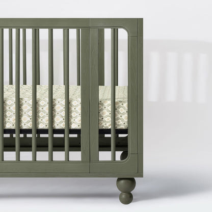 Babyletto olive green wooden crib with patterned mattress sheet
