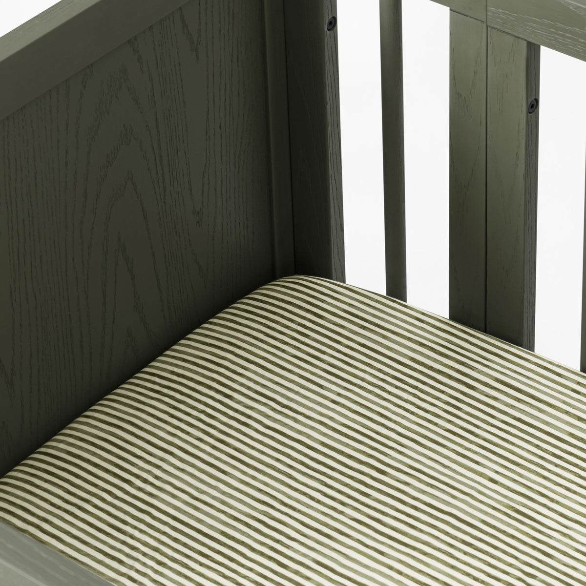 Close up of Babyletto crib corner with dark wood frame and striped mattress