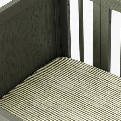 Close up of Babyletto crib corner with dark wood frame and striped mattress