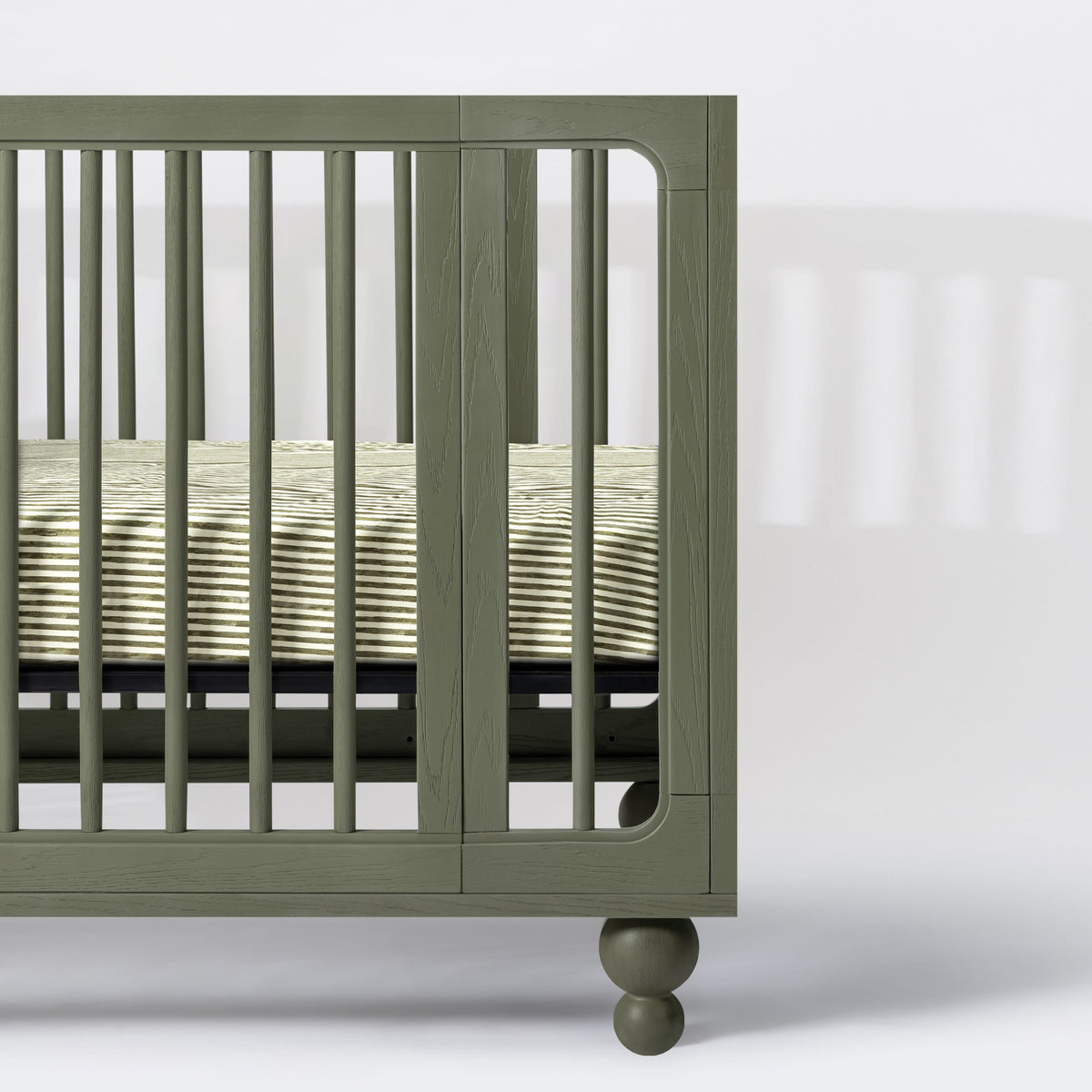 Babyletto olive green wooden crib side view with striped mattress sheet