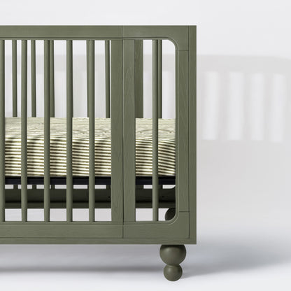 Babyletto olive green wooden crib side view with striped mattress sheet
