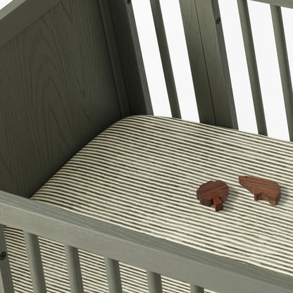 Babyletto crib with striped mattress sheet and two small wooden animal figures