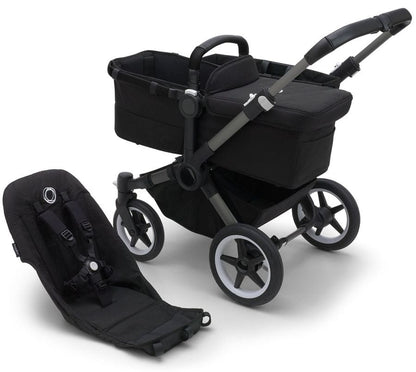 Graphite and midnight black Donkey 5 base by Bugaboo with matching carrycot and infant seat, featuring sleek black fabric, silver accents, and white-rimmed wheels, shown in studio view.