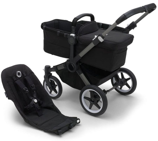 Graphite and midnight black Donkey 5 base by Bugaboo with matching carrycot and infant seat, featuring sleek black fabric, silver accents, and white-rimmed wheels, shown in studio view.