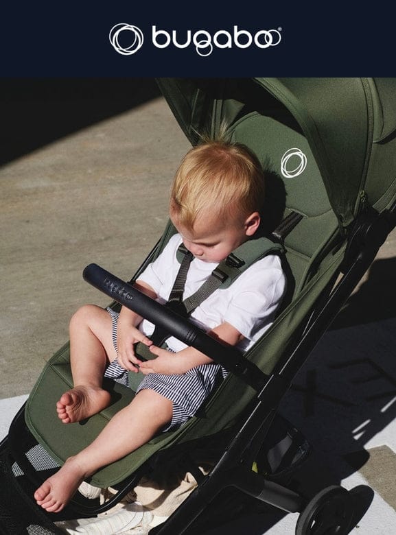 Toddler in white shirt and striped shorts sits in olive green Bugaboo stroller, barefoot, under bright sunlight.