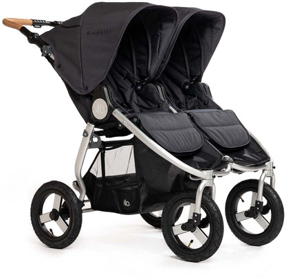 Dark gray side-by-side double stroller by Bumbleride with silver frame, wooden handle, black wheels, and mesh storage basket, front three-quarter view