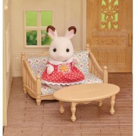 Sylvanian Families rabbit figure wearing a red polka dot dress sitting on a miniature sofa with a coffee table