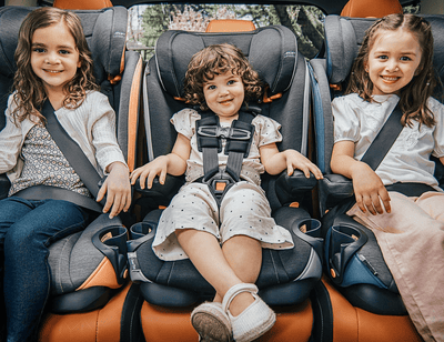 Three children seated in car seats in the back of a vehicle