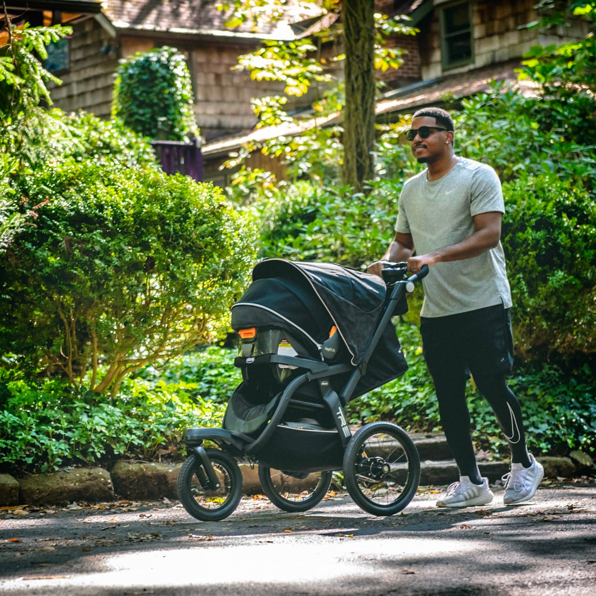 Man pushing a black Chicco jogging stroller on a paved path