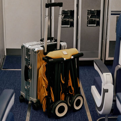 Folded mustard yellow Cybex Libelle stroller leaning against a silver carry on suitcase in an airplane aisle