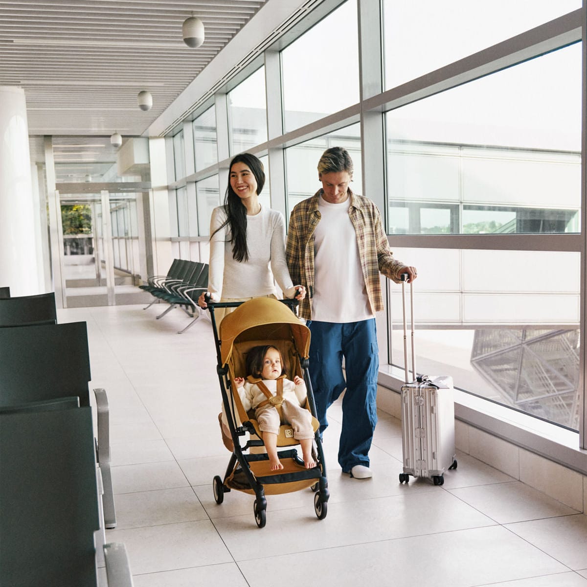 Parents walking through an airport terminal with a child in a Cybex stroller and a rolling suitcase