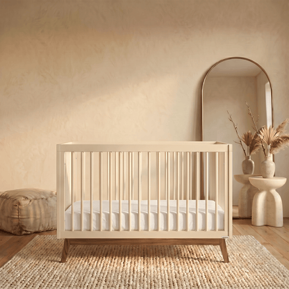 Dadada crib with light wooden frame and white mattress on a textured rug in a neutral room