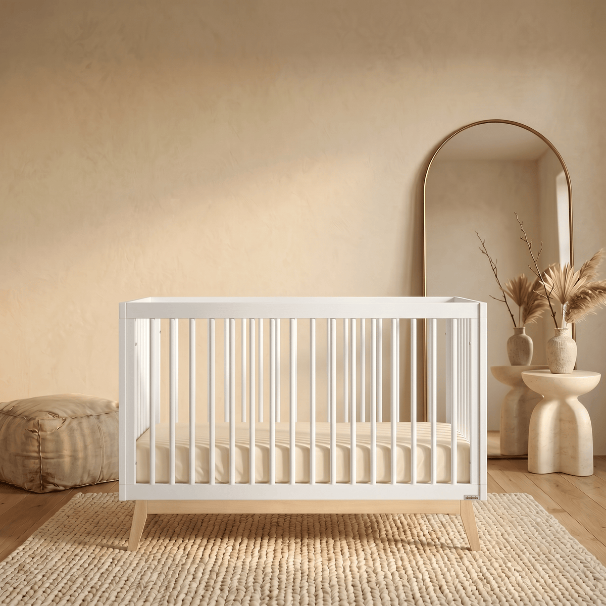 Dadada white crib with light wood legs on a textured rug in a neutral room