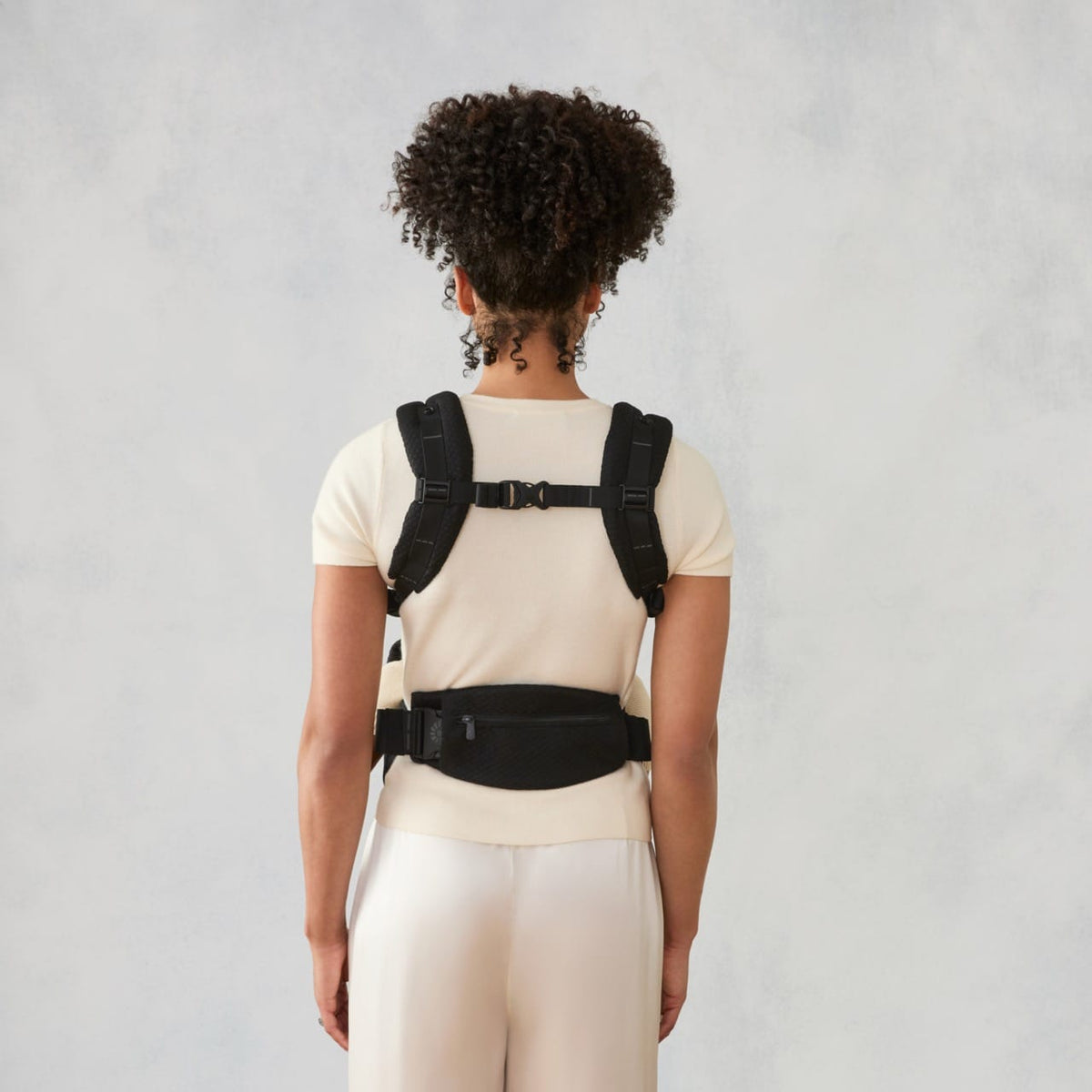 Back view of person wearing black Ergobaby baby carrier with waist belt and shoulder straps