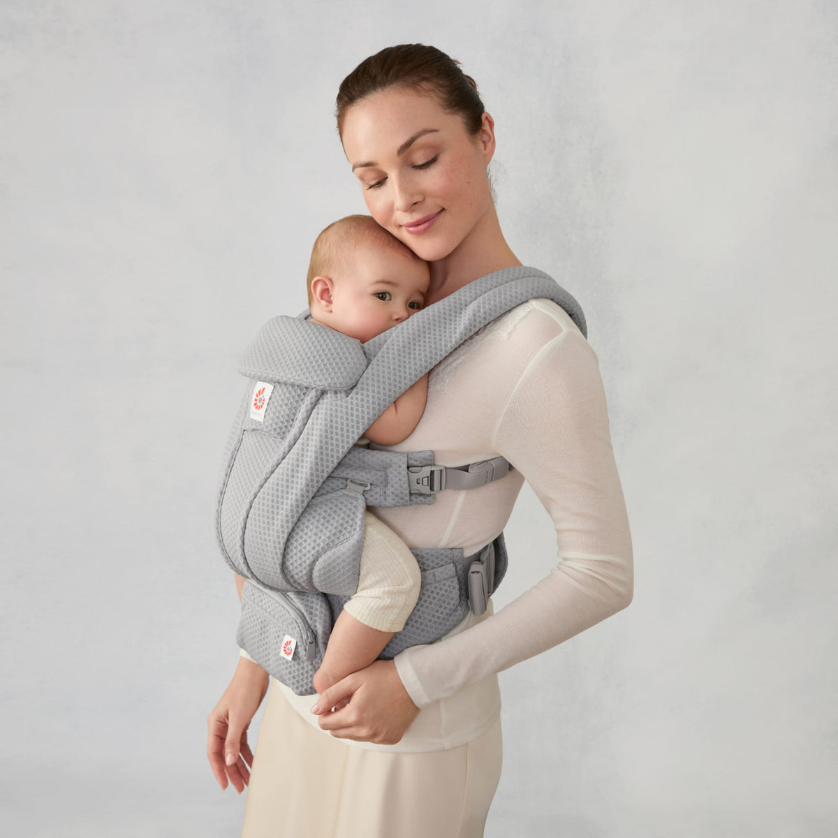 Woman wearing a grey Ergobaby Omni Breeze baby carrier with an infant facing inward