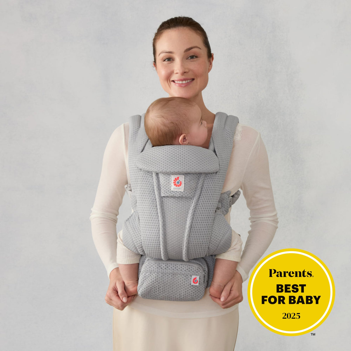 Woman wearing a grey Ergobaby carrier with a baby and a Parents Best for Baby 2025 award badge
