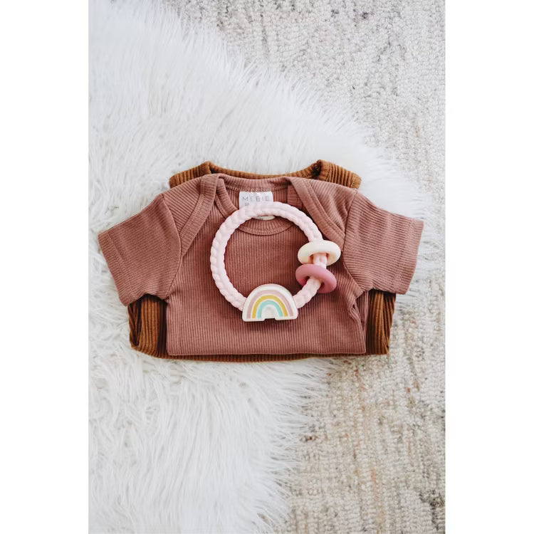Itzy Ritzy rainbow silicone teether on top of folded ribbed baby bodysuits