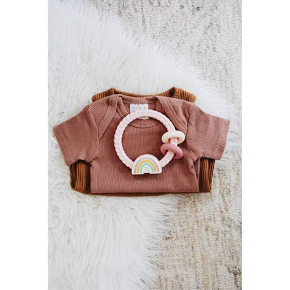 Itzy Ritzy rainbow silicone teether on top of folded ribbed baby bodysuits