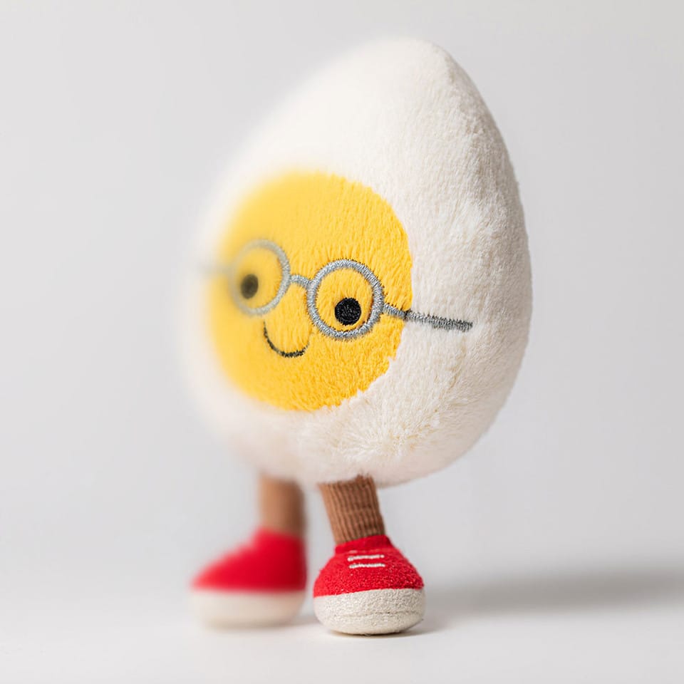 Jellycat plush toy shaped like a hard boiled egg with embroidered glasses and red sneakers