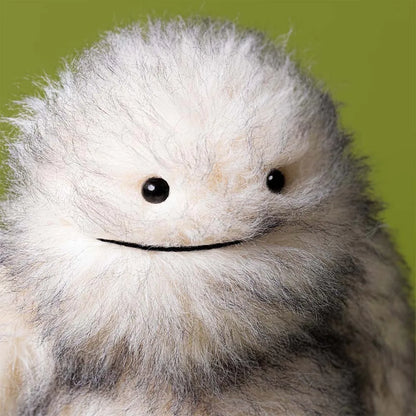 Jellycat plush toy with white shaggy fur and black bead eyes against a green background