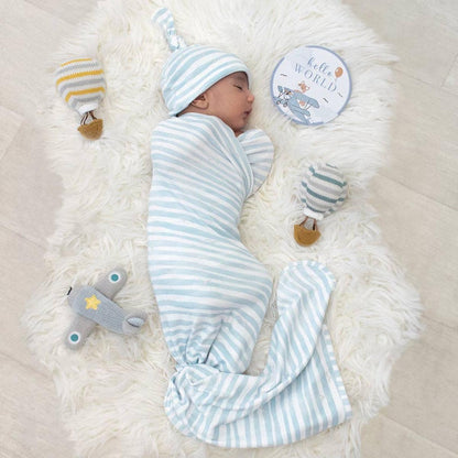 Baby in Living Textiles blue striped swaddle and hat on a white faux fur rug with airplane toys and hello world sign