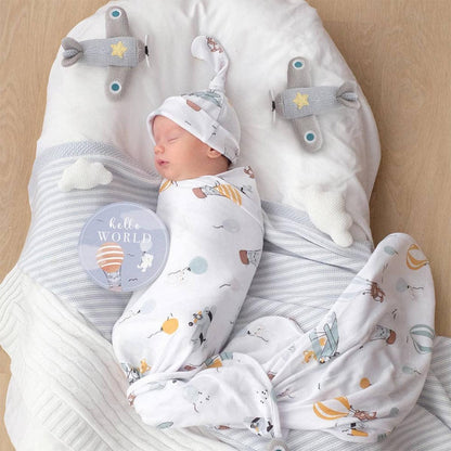 Newborn swaddled in Living Textiles airplane print wrap and matching hat in a baby nest