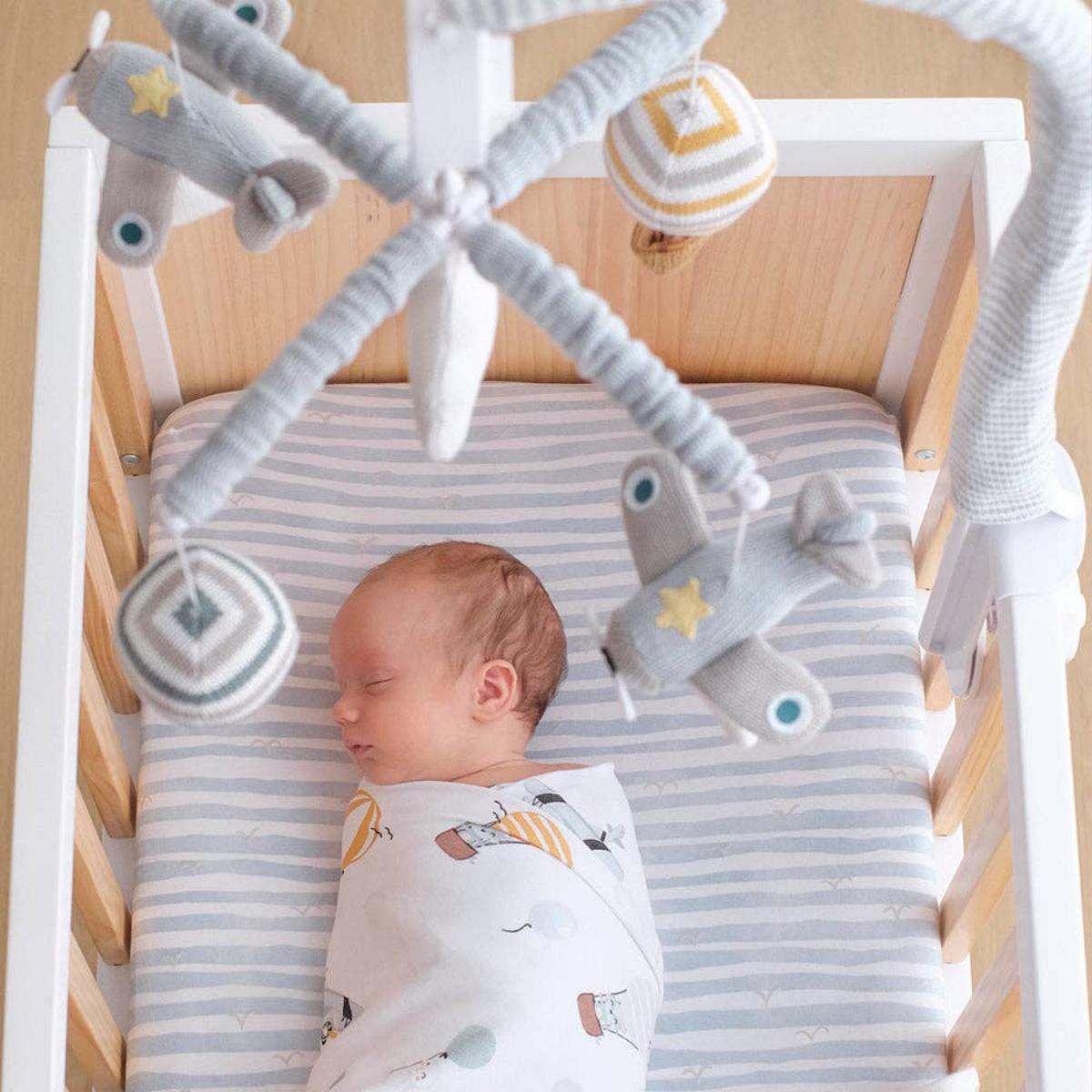 Newborn sleeping in a crib with a Living Textiles airplane mobile overhead