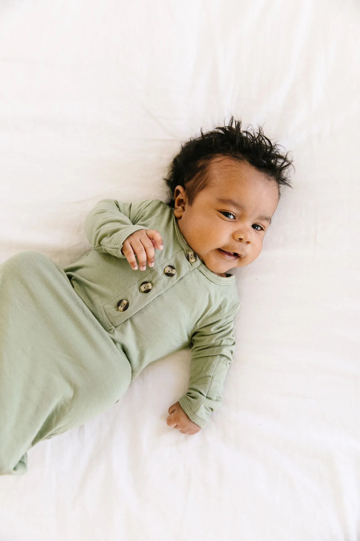 Baby wearing a sage green Lou Lou and Company button down sleeper on a white blanket