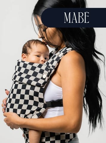 Woman with long black hair carries baby in black-and-white checkered MABE baby carrier, white background.