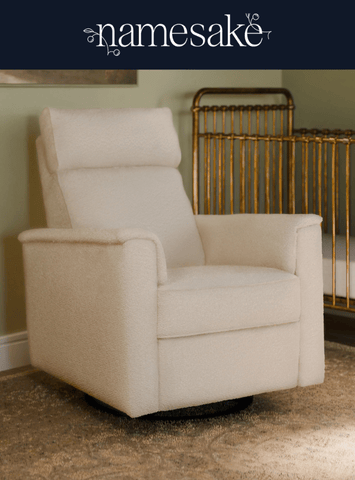 A cream-colored, upholstered armchair rests on a patterned rug, with a brass-colored crib in the background. The word "namesake" is visible in script at the top.
