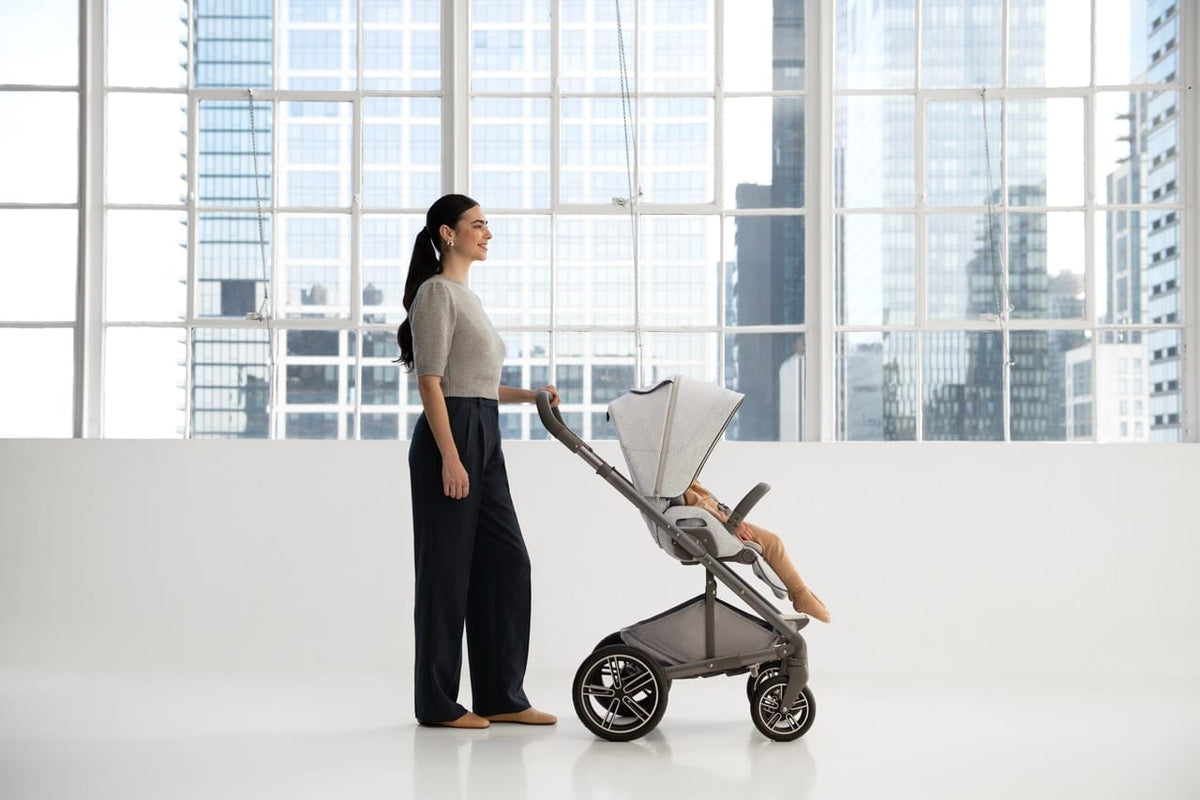 Woman pushing a grey Nuna stroller with a child inside in a bright room with large windows