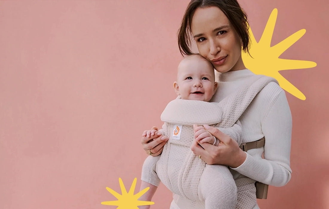 Woman wearing a Baby Carrier with a baby in it, facing out. Save at Albee, limited time sale