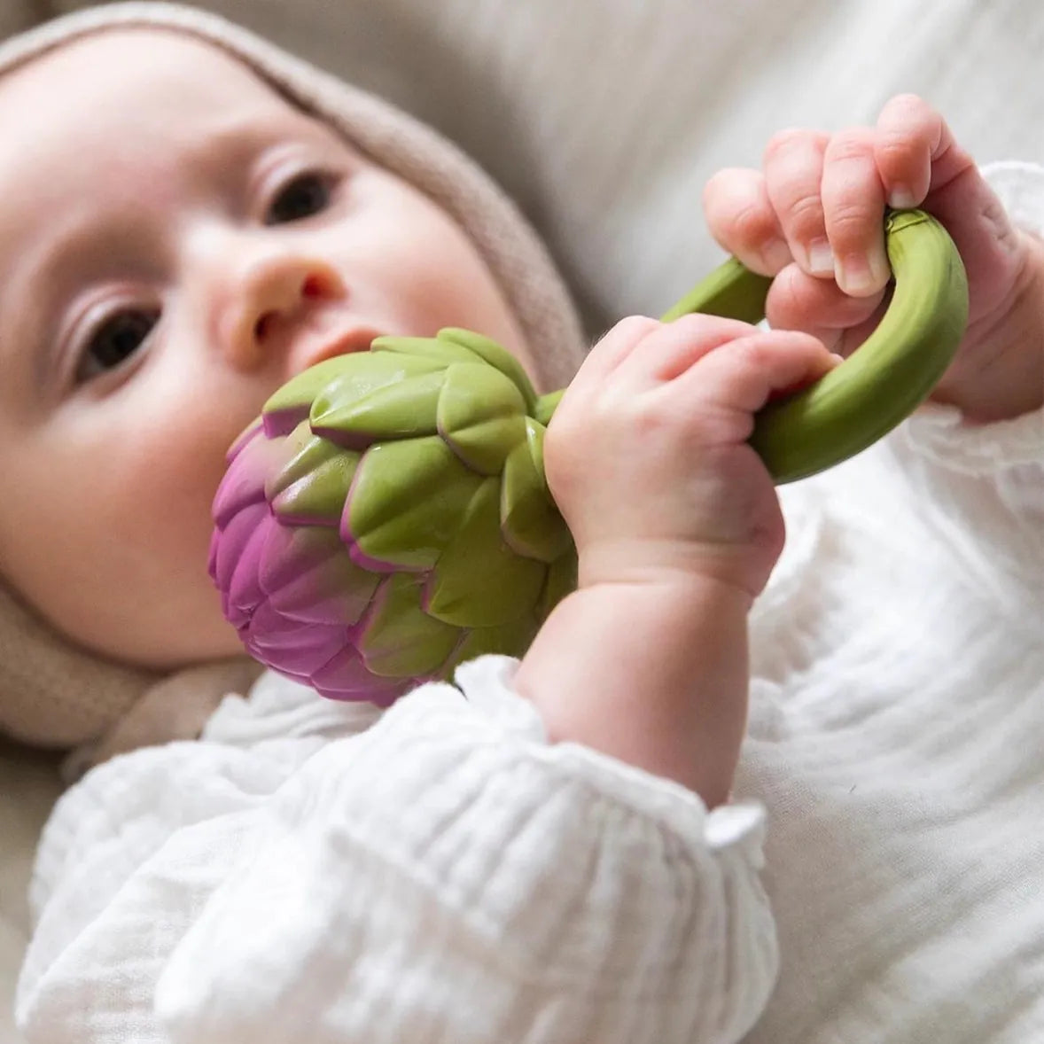 Baby holding a green and purple artichoke shaped silicone teether