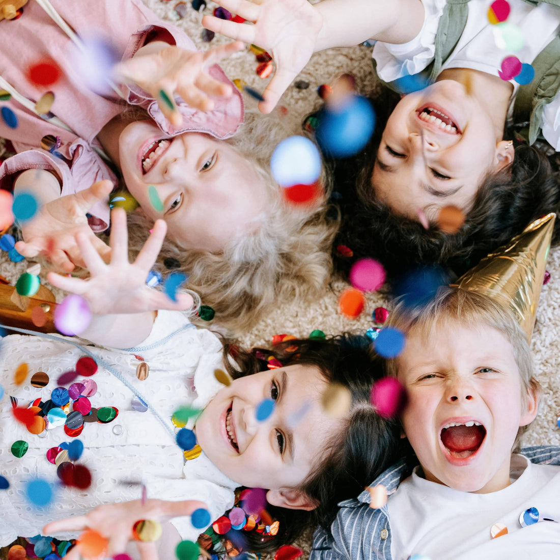 Four children lying on the floor covered with colorful confetti - by ivan samkov from pexels