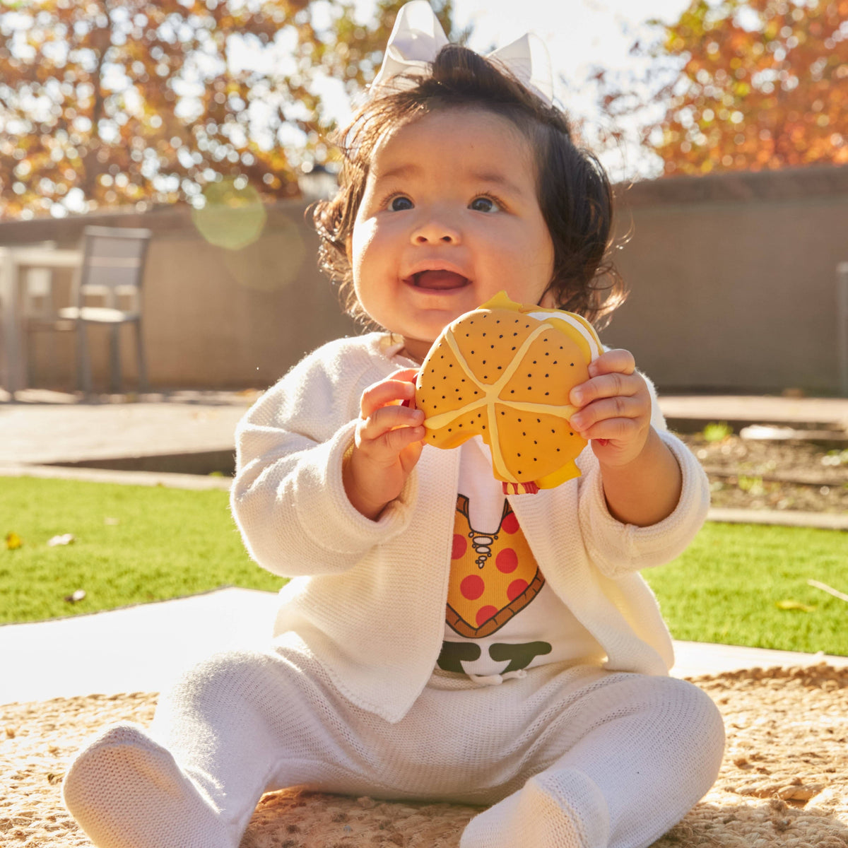 Baby sitting on a mat holding a yellow pizza slice teether toy