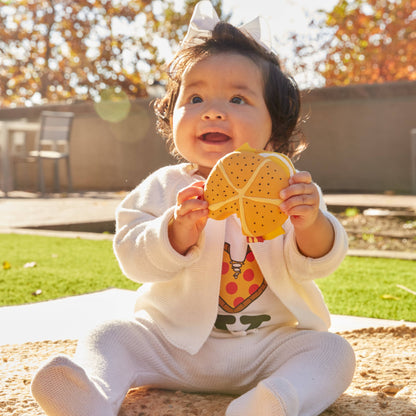 Baby sitting on a mat holding a yellow pizza slice teether toy