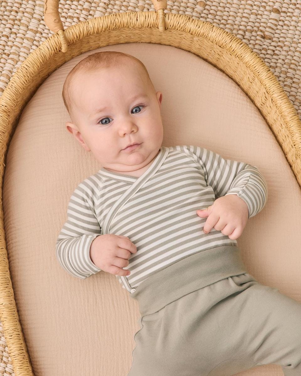 Baby wearing Quincy Mae striped long sleeve wrap bodysuit and solid green pants in a woven basket