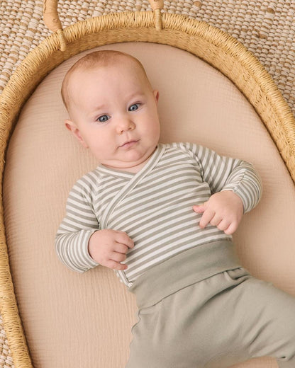 Baby wearing Quincy Mae striped long sleeve wrap bodysuit and solid green pants in a woven basket