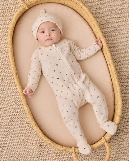 Baby wearing Quincy Mae cream floral footie and matching hat lying in a woven bassinet