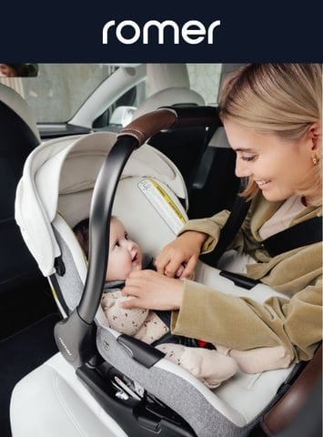 Mother gently touches baby in Romer car seat inside vehicle, soft lighting, beige and gray tones, brand logo visible.
