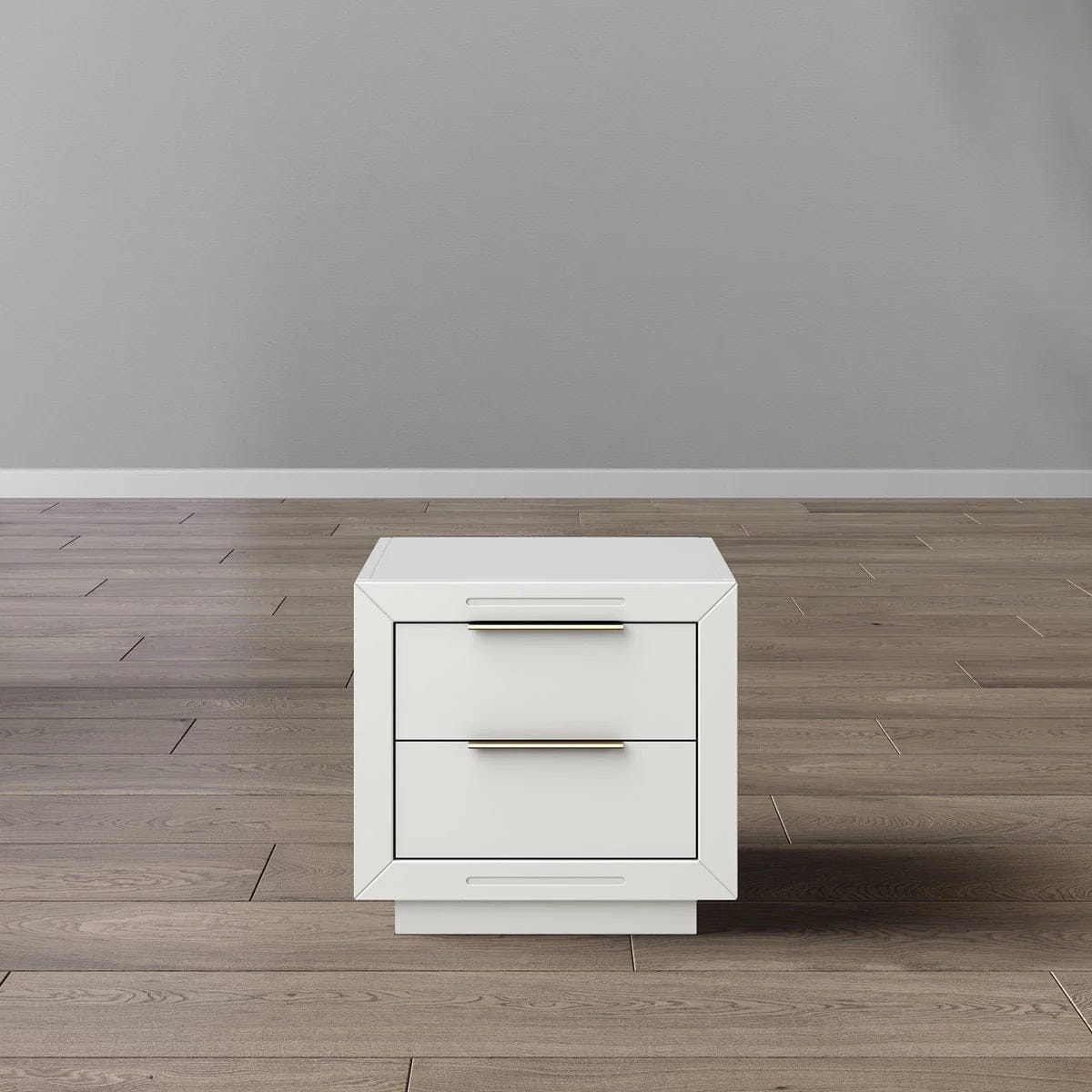 White nightstand with two drawers and gold handles on a wooden floor against a gray wall.