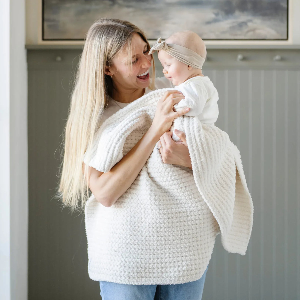 Woman holding a baby wrapped in a cream Saranoni textured blanket