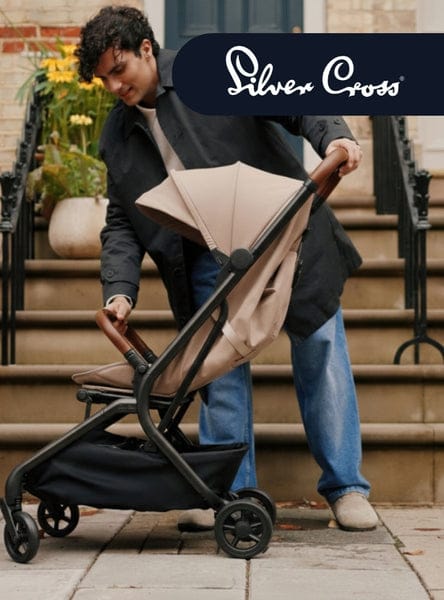 A person folds a tan and black stroller on a stone sidewalk. Text on the top right reads "Silver Cross."
