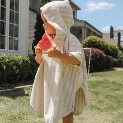 Toddler wearing a striped hooded Snuggle Me Organic towel poncho eating a slice of watermelon outdoors