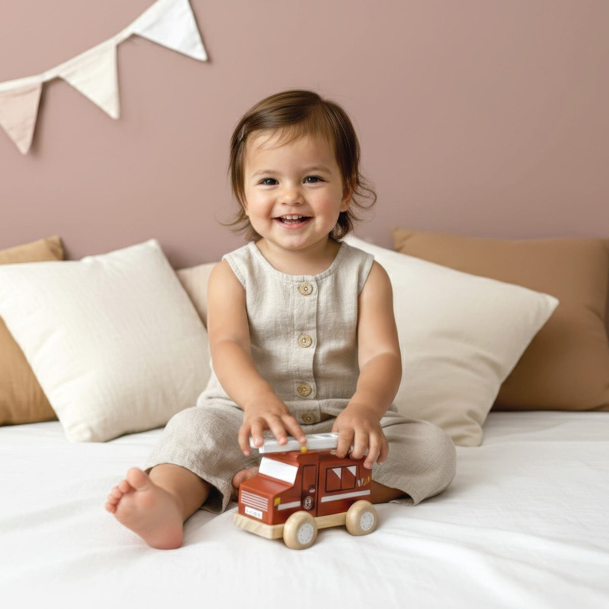 Toddler playing with a Speedy Monkey wooden fire engine toy on a bed