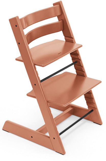 Terracotta high chair by Stokke with slatted back, adjustable height, black safety bars, side view on white background