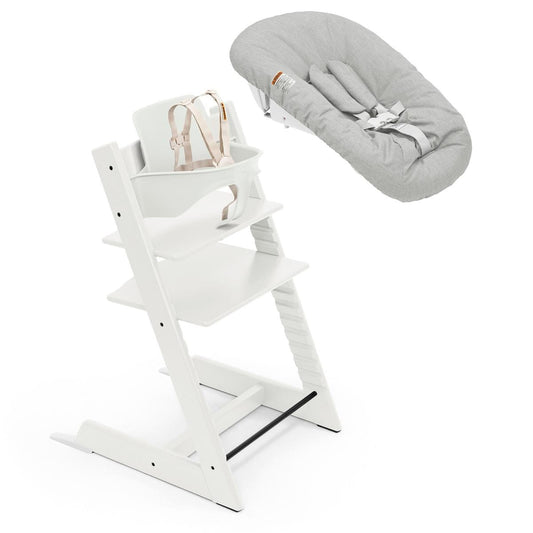 White wooden high chair with beige harness and grey newborn set by Stokke, shown in open box view with adjustable legs and safety straps.