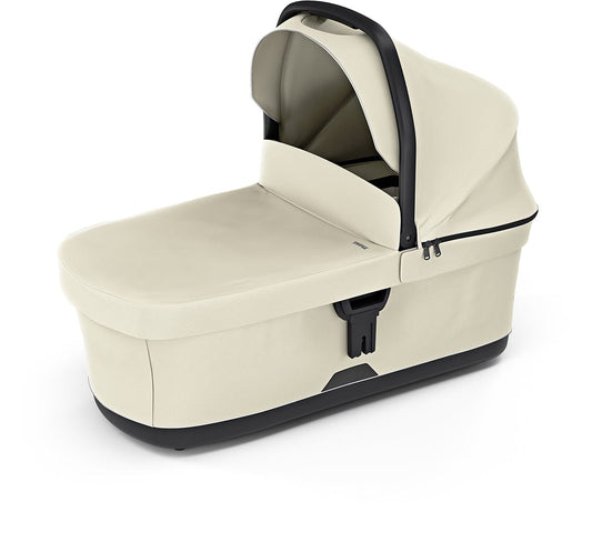 Soft beige Thule OPEN BOX bassinet with black trim and canopy, side view, textured fabric, secure latches, and ergonomic handle