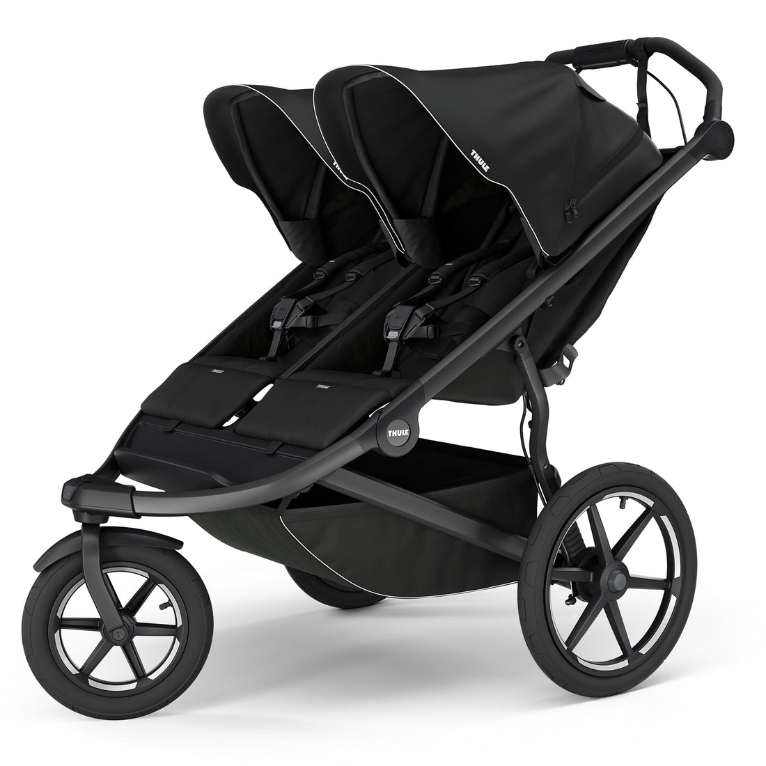 Black double jogging stroller by Thule with magnetic buckle, side view, large all-terrain wheels, padded seats, and white trim accents